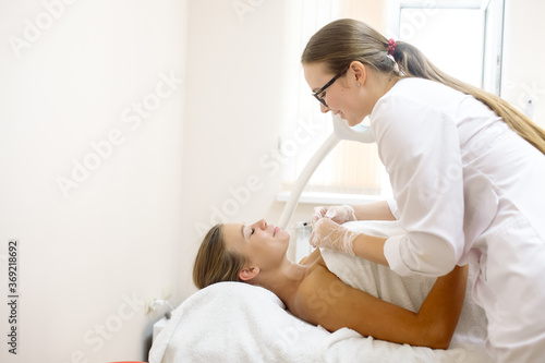 The beautician makes the patient's chin shape correction using injections of hyaluronic acid filler