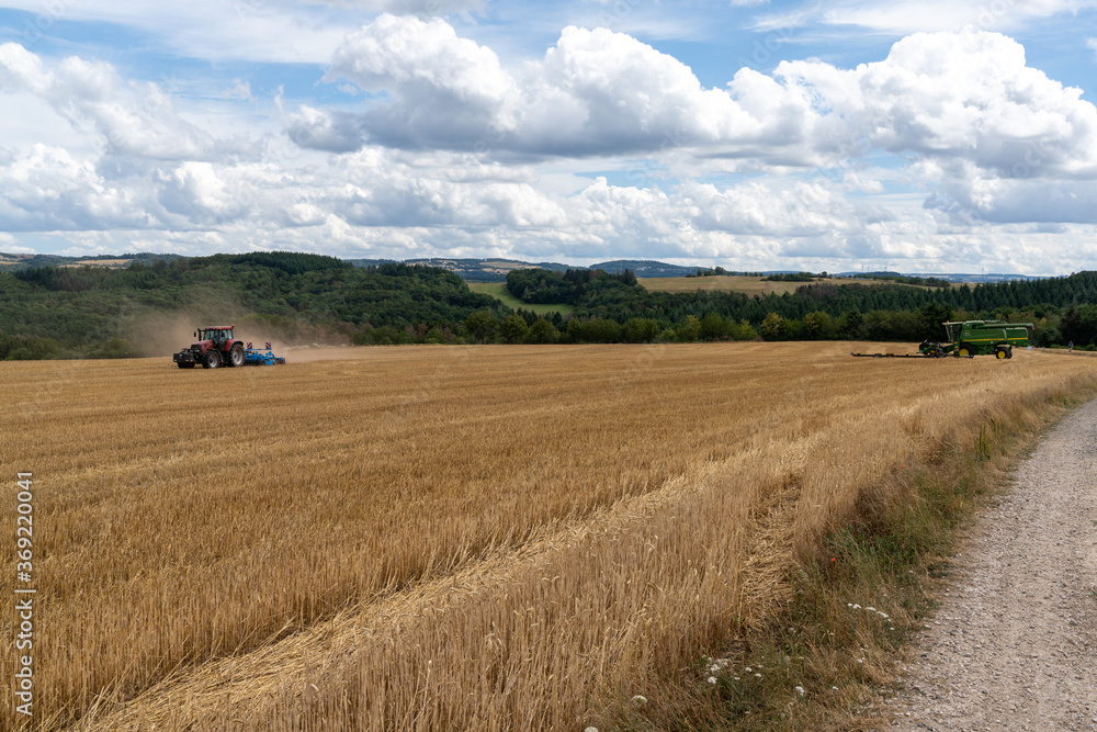 red tractor pulling a blue field cultivator across a harvested wheat field with a combine in the back ground