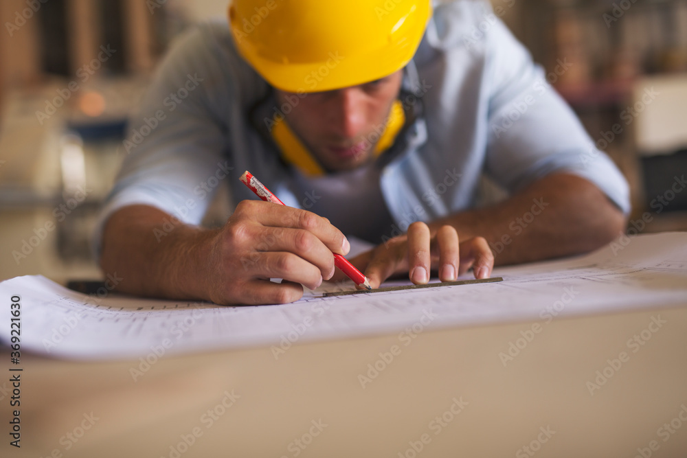 Young carpenter underlining blueprint using pencil and a ruler Young carpenter underlining blueprint using pencil and a ruler