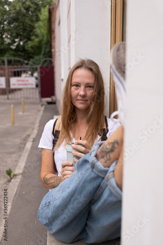 a beautiful smiling girl in a white t-shirt and jeans poses on the streets of the city. she has long hair and no makeup. the architecture of the old city is a backdrop around it. High quality photo