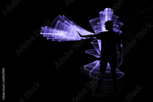 Silhouette of a man standing in front. Abstract shape with light saber in the background. Lightpainting scene.
