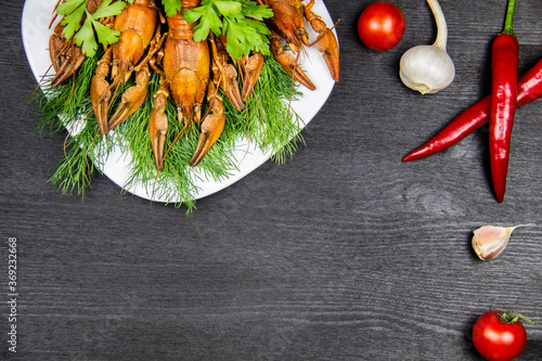 Red boiled crawfish on a white plate with a dill and parsley on the dark wood background. Cooking food background with free space for text.  Top view with copy space