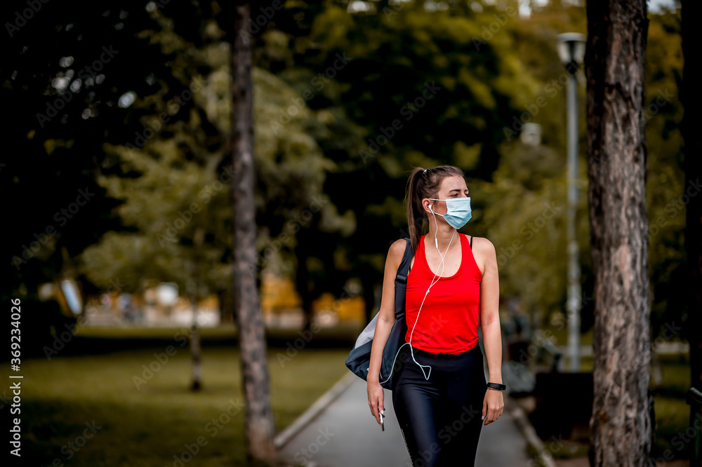 Naklejka premium Young Caucasian woman with protective face mask on her way to training in a public park.