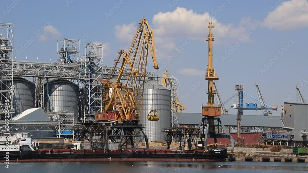 Odesa, Ukraine. Yellow harbor cranes unload a barge at the Odessa International Seaport amid large metal tanks. Big cargo port at sea, delivery, unloading of ships, storage of goods Odesa, Ukraine. Yellow harbor cranes unload a barge at the Odessa International Seaport amid large metal tanks. Big cargo port at sea, delivery, unloading of ships, storage of goods