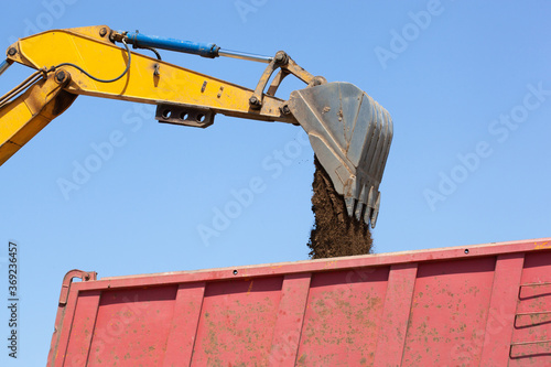 bucket of an excavator pouring rock on the back of a truck