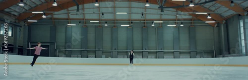 Professional teenager figure skater parcticing with his trainer on ice. Shot on RED cinema camera with 2x Anamorphic lens, 75 FPS Slow motion photo