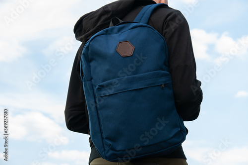 Close up of blue backpack on mans back on sky background, mock up, place for text
