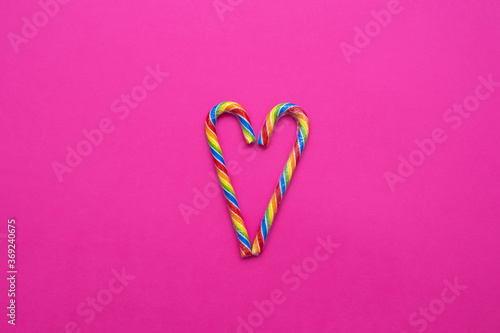 multicolored candy canes in the form of a heart on a pink background  copy space