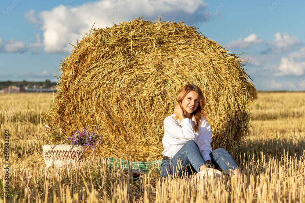 Beautiful young woman in a white shirt and jeans resting in a field near a hay bale. Beautiful young woman in a white shirt and jeans resting in a field near a hay bale.