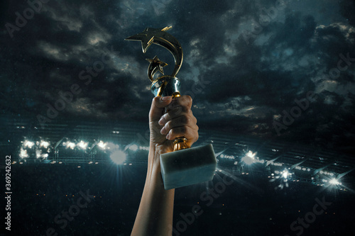 Hard work. Award of victory, male hands tightening the golden cup of winners against cloudy dark sky. Sport, competition, championship, winning, achieving the goal. Prize for success and honor.