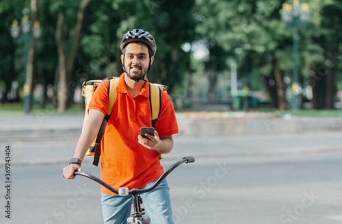 Cyclist with delivery. Happy courier with backpack, smart watch and smartphone, sits on bicycle