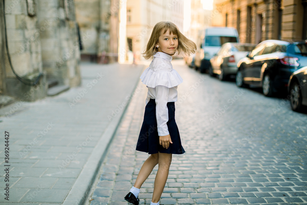 Naklejka premium Happy little child, adorable blonde girl in black and white business wear, walking on old city street in ancient European city on sunny summer morning
