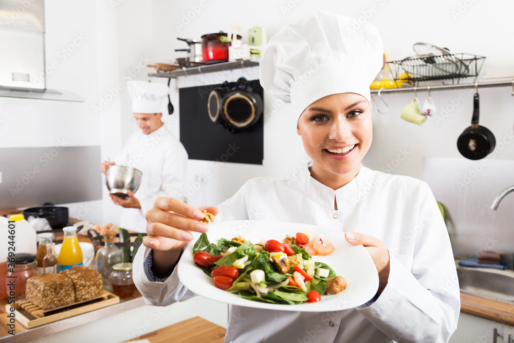Smiling woman chef serving fresh salad at restaurant's kitchen
