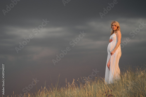 Pregnant woman in white dress posing in the park against the dark sky