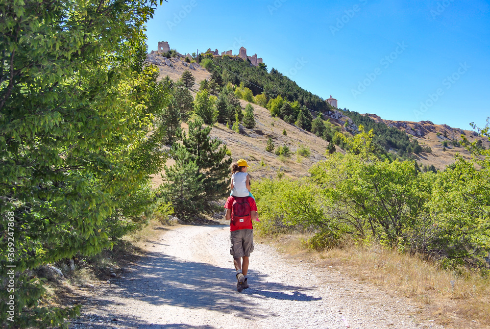 Dad with little child on his shulders walking on a path towards Rocca Calascio, mountaintop fortress in the Gran Sasso and Monti della Laga National Park, province of L'Aquila, Abruzzo region, Italy.