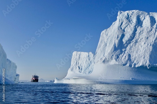 Cruise ship between icebergs in antarctic ocean, blue sky, sun, Antarctica