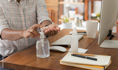 Female worker sit in home office use hand sanitizer against coronavirus pandemic work with computer and coffee on table..