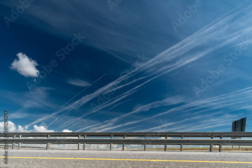 White traces of condensation of water vapor in the form of lines from flying planes over the highway, over the field and trees. 