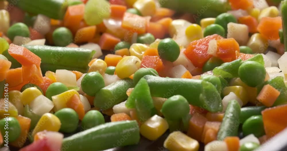 a mix of different frozen vegetables is prepared in a preheated pan. macro photography in the studio. movement of the camera using the slider. a mix of different frozen vegetables is prepared in a preheated pan. macro photography in the studio. movement of the camera using the slider.