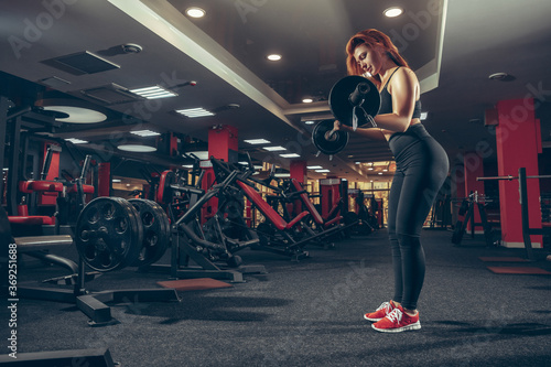 Strong. Young muscular caucasian woman practicing in gym with equipment. Athletic female model doing exercises, training her upper body, working out with barbell. Wellness, healthy lifestyle
