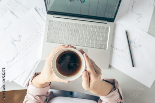 Top view. Business woman sitting at table with cup of coffee and working  with graphics and charts printed on the paper. Top view