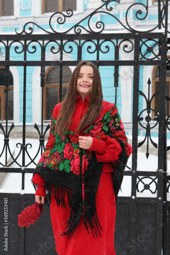 Retro style architectural fashion. Russian girl in vintage folk Pavlovo Posad shawl, scarf, stylish red coat. Architecture of old center in Moscow city, Russia. Gate of Chertkov's house. Snow winter photo