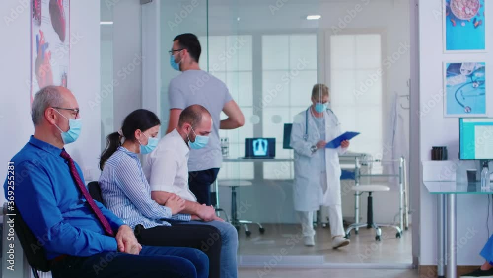 Senior doctor giving bad news to young couple in hospital waiting area. Medic in white coat wearing face mask against infection with coronavirus. Nurse with visor. Senior doctor giving bad news to young couple in hospital waiting area. Medic in white coat wearing face mask against infection with coronavirus. Nurse with visor.
