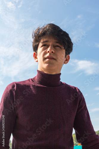 a young guy of Eastern appearance with black hair and a handsome expressive face poses in a Park against the background of trees and architecture. High quality photo