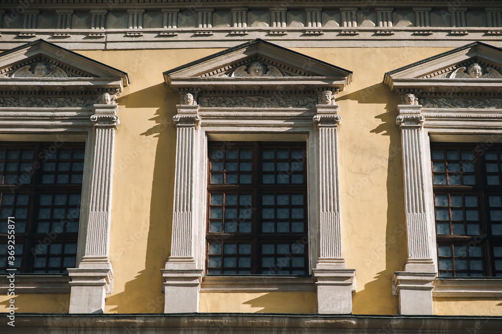 Windows on the facade of a house with beige plaster in the central historical part of the city. Beautiful decorative architecture with reliefs, cornice and white columns in Lviv, Ukraine.