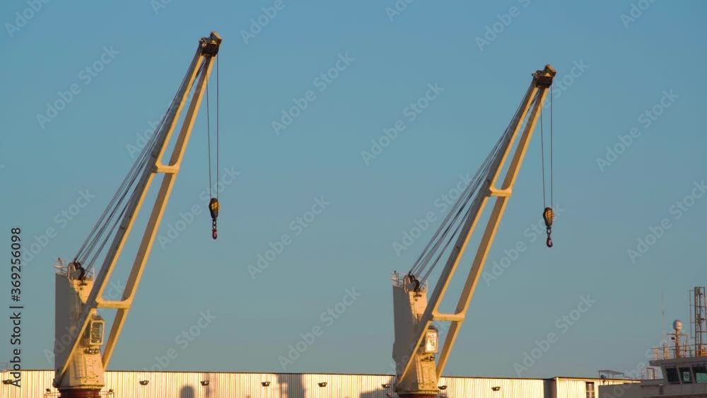 Port cranes heavy lifts in the port on sunny day against blue sky background, close up view. Shipment, export, import busines. Port cranes heavy lifts in the port on sunny day against blue sky background, close up view. Shipment, export, import busines.