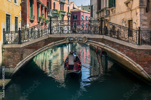 A lonely gondola navigating the water channel and passing slowly below a bridge near San Marco in the center of Venice