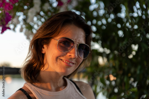 Beautiful woman wearing sunglasses at sunset by the river. Beauty and Fashion luxury style. Selective focus on the sunglasses