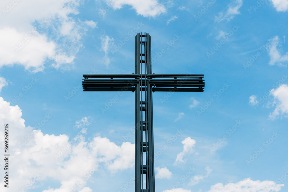 Fototapeta premium Big metal christian cross high in the blue sky. Symbol of love for Jesus. Catholic church monumental construction.