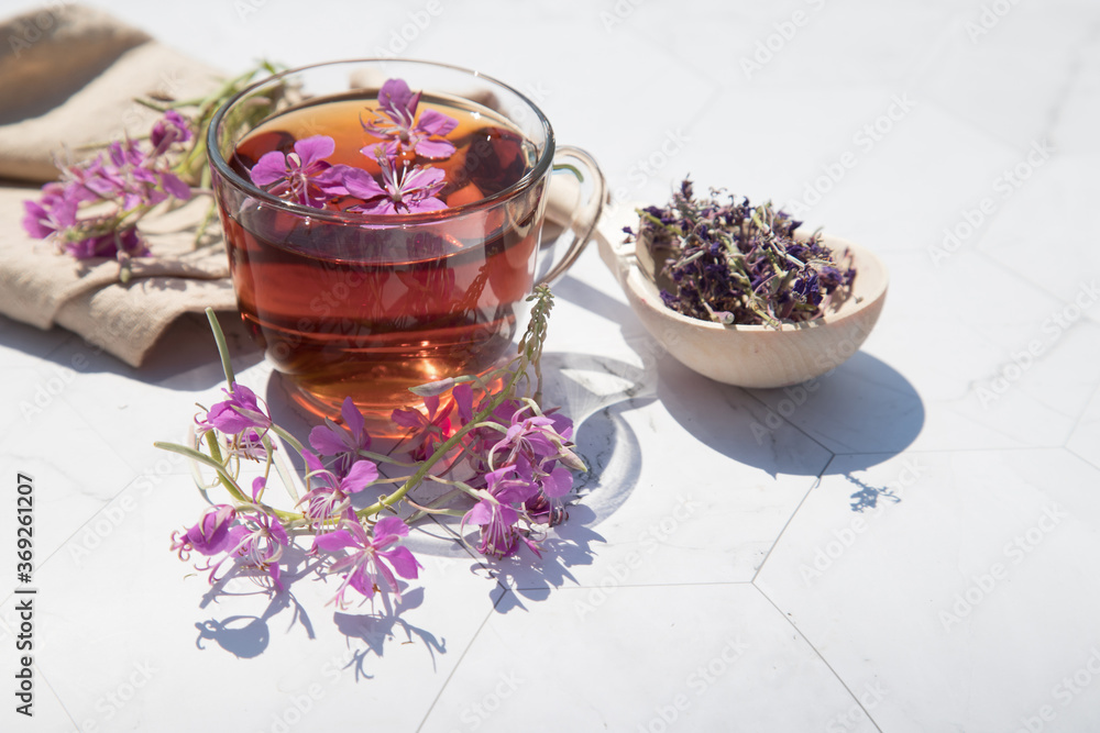 Herbal tea from fermented kipreya leaves in a glass Cup on a light background, dried flowers lie in a wooden spoon next to it.Traditional Russian Kopor Tea (Ivan-Tea). Place for a copy of space Herbal tea from fermented kipreya leaves in a glass Cup on a light background, dried flowers lie in a wooden spoon next to it.Traditional Russian Kopor Tea (Ivan-Tea). Place for a copy of space