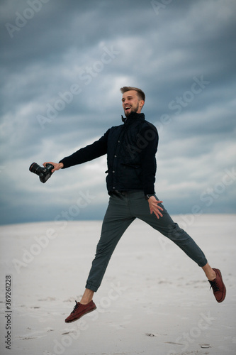 Photographer has a fun, jumps and laughs in desert with digital camera in his hand.