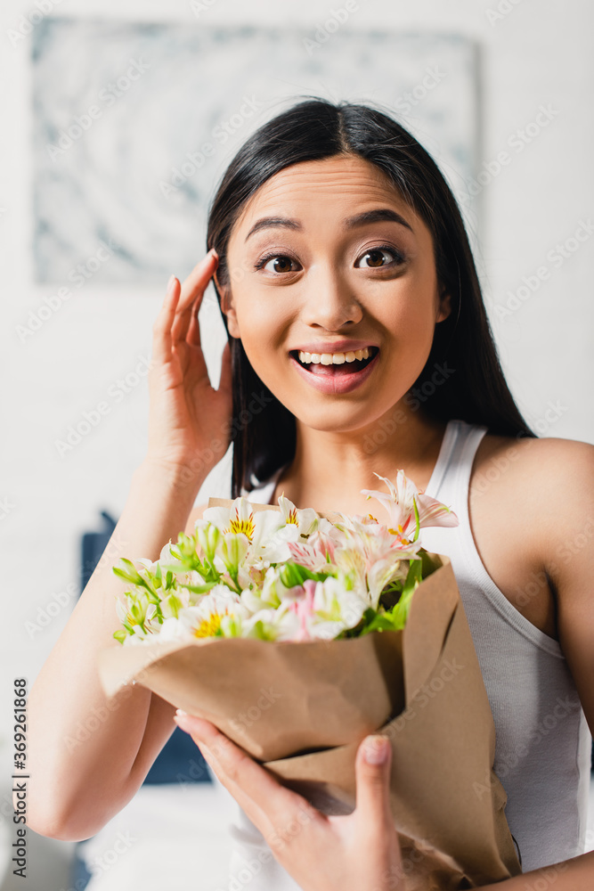 Selective focus of cheerful asian girl holding bouquet and looking at camera at home Selective focus of cheerful asian girl holding bouquet and looking at camera at home