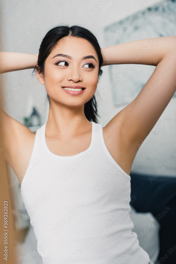 Selective focus of cheerful asian girl looking away in bedroom