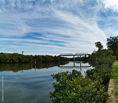 Beautiful view of a river with reflections of a tall pedestrian and water pipe  bridge, trees, deep blue sky and puffy clouds on water, Parramatta river, Rydalmere, Sydney, New South Wales, Australia
