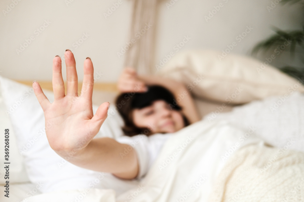 Young beautiful girl lying in comfortable bed wearing sleep mask in the morning at cozy room. Concept of rest at home, sleep, insomnia, self-isolation, stay home during quarantine, pandemic.