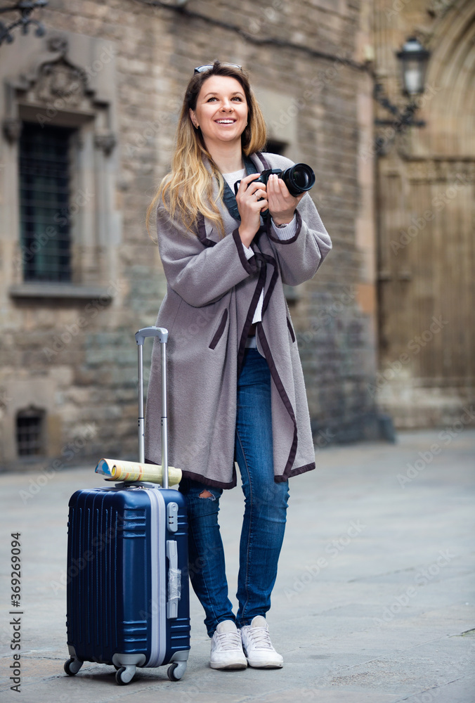 Blond positive girl holding camera in hands and photographing in the city