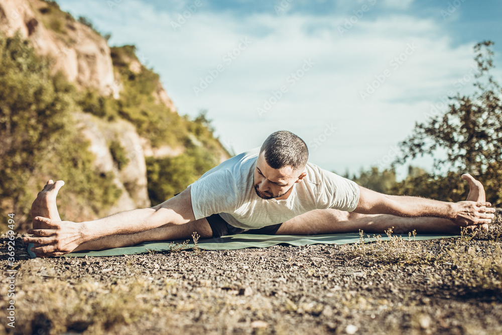 Young fitness man doing yoga exercise outdoors at the quarry lake. Handsome young man with a beard doing yoga exercise.