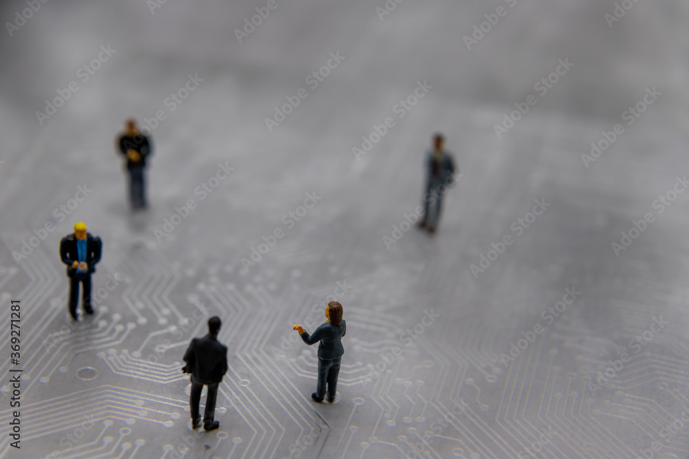 Miniature figurines posed as business people in a meeting over abstract futuristic circuit board, future business concept Miniature figurines posed as business people in a meeting over abstract futuristic circuit board, future business concept