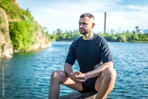 Bearded young man sitting on the rocks on the quarry lake background. Handsome portrait.