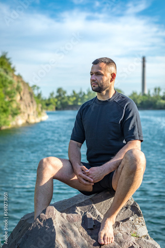 Bearded young man sitting on the rocks on the quarry lake background. Handsome portrait. © Inception
