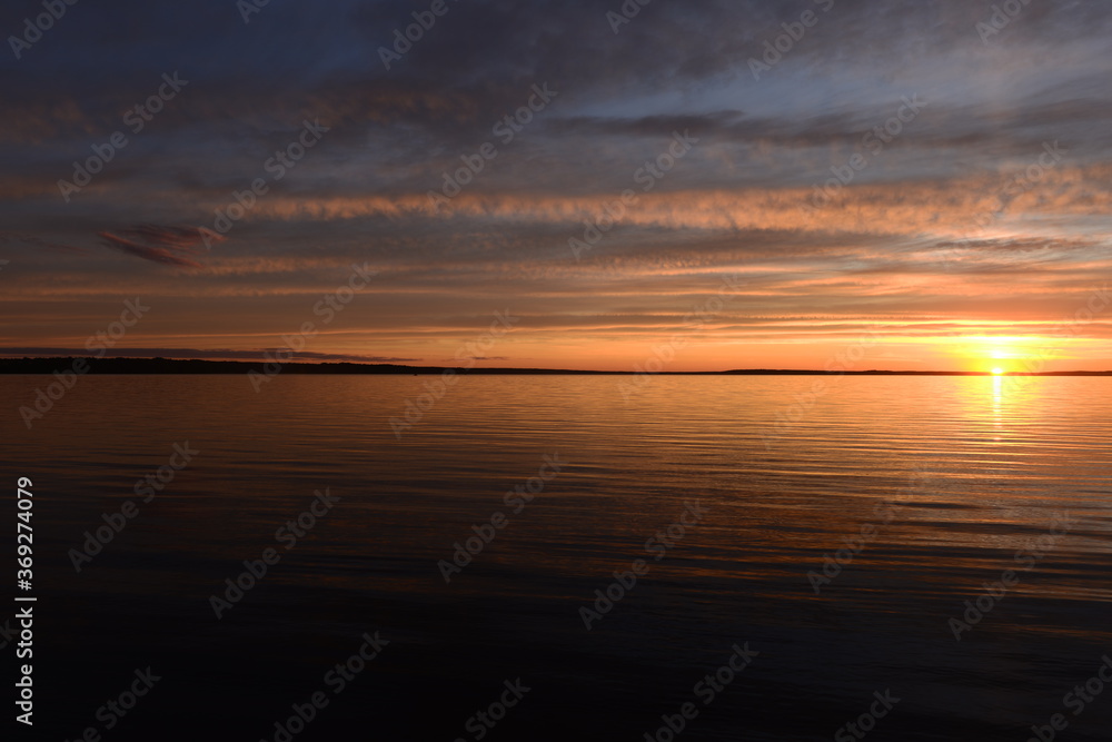 Brightly glow sunbeam  on the horizon over the lake water surface at sunset