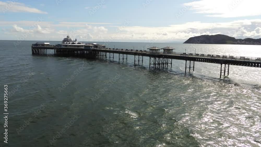 Aerial view historic Llandudno pier landmark tourist seaside promenade landmark dolly left above ocean waves Aerial view historic Llandudno pier landmark tourist seaside promenade landmark dolly left above ocean waves