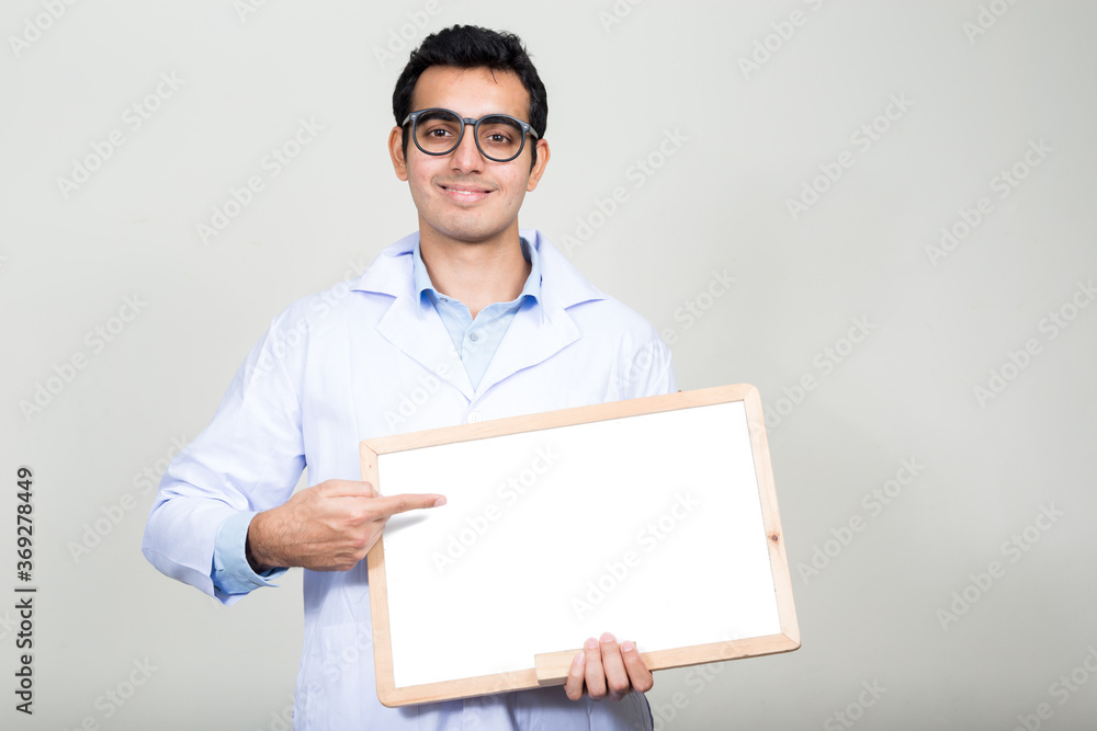 Portrait of happy young handsome Indian man doctor showing white board Portrait of happy young handsome Indian man doctor showing white board
