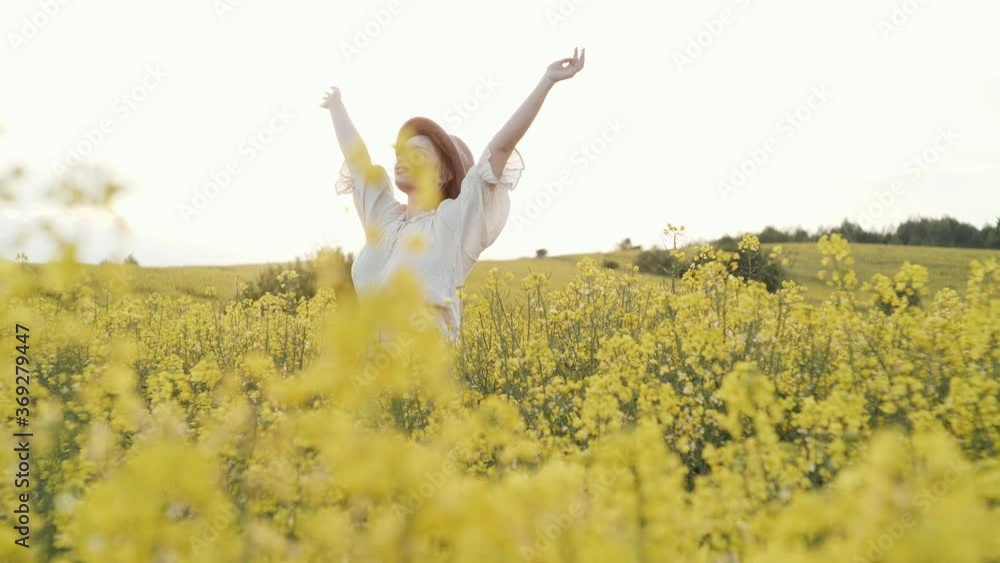 Happy Charming woman putting on her Hands while standing at the Field full of Yellow Flowers. Wearing trendy Light Clothes. Having brown Hat. Looking Happy and feeling Liberty at Countryside. Happy Charming woman putting on her Hands while standing at the Field full of Yellow Flowers. Wearing trendy Light Clothes. Having brown Hat. Looking Happy and feeling Liberty at Countryside.