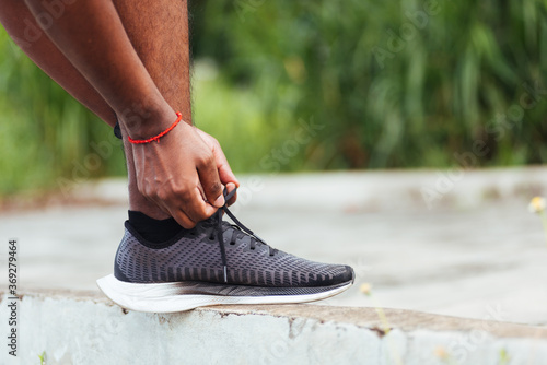 Close up Asian sport runner black man wear watch stand step on the footpath trying shoelace running shoes getting ready for jogging and run outdoor street health park  healthy exercise workout concept