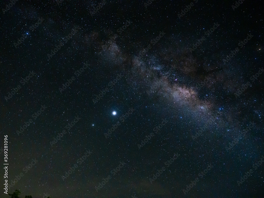 Fototapeta premium Beautiful night sky of Milky Way and many stars on a dark night above green trees and light from rural village at Suan Phueng, Ratchaburi, Thailand.
